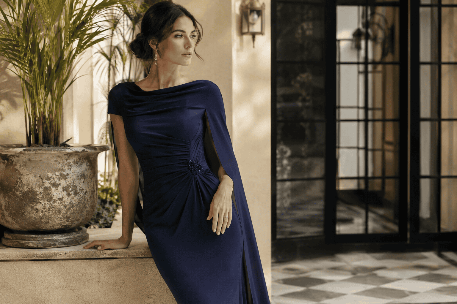 A woman in a navy draped gown standing in a sunlit courtyard